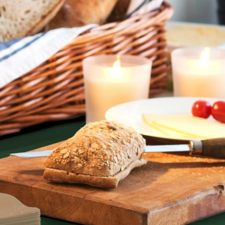 Frokostbord, med oppskjært brød på en fjøl og levende lys i bakgrunnen
